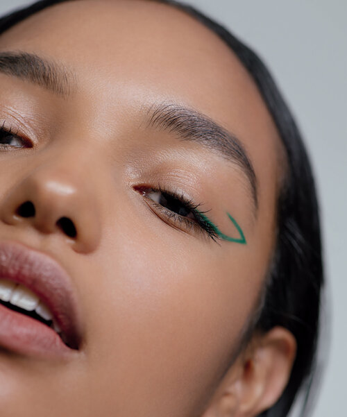 Close-up studio shot of a young adult woman with tan skin, featuring an eye-level view and green eyeliner.
