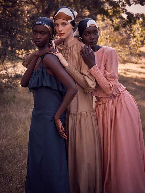 Three women pose outdoors wearing headscarves and long dresses in complementary neutral tones; fashion editorial.