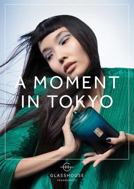 Asian woman with long black hair and bright blue eyeliner holds a dark blue candle holder with gold accent in a studio shot.