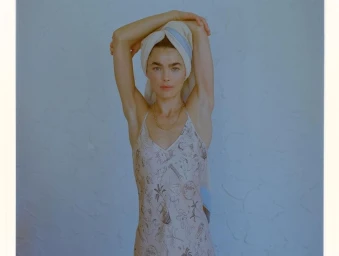 Woman in a printed slip dress with a towel wrapped around her head posing against a pale textured background