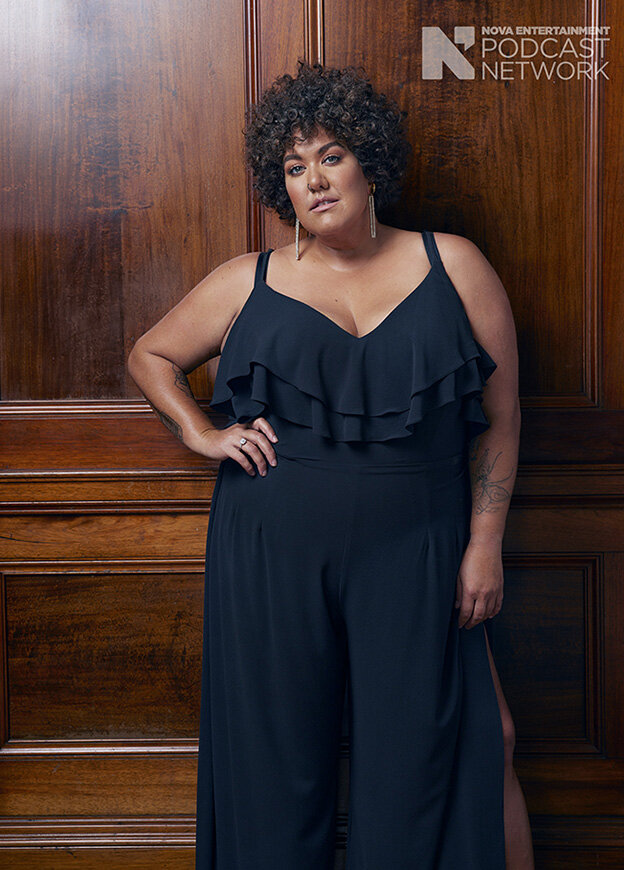 Portrait of an adult woman with curly hair wearing a black jumpsuit, posing in front of a dark wooden door. Podcast Network logo visible.