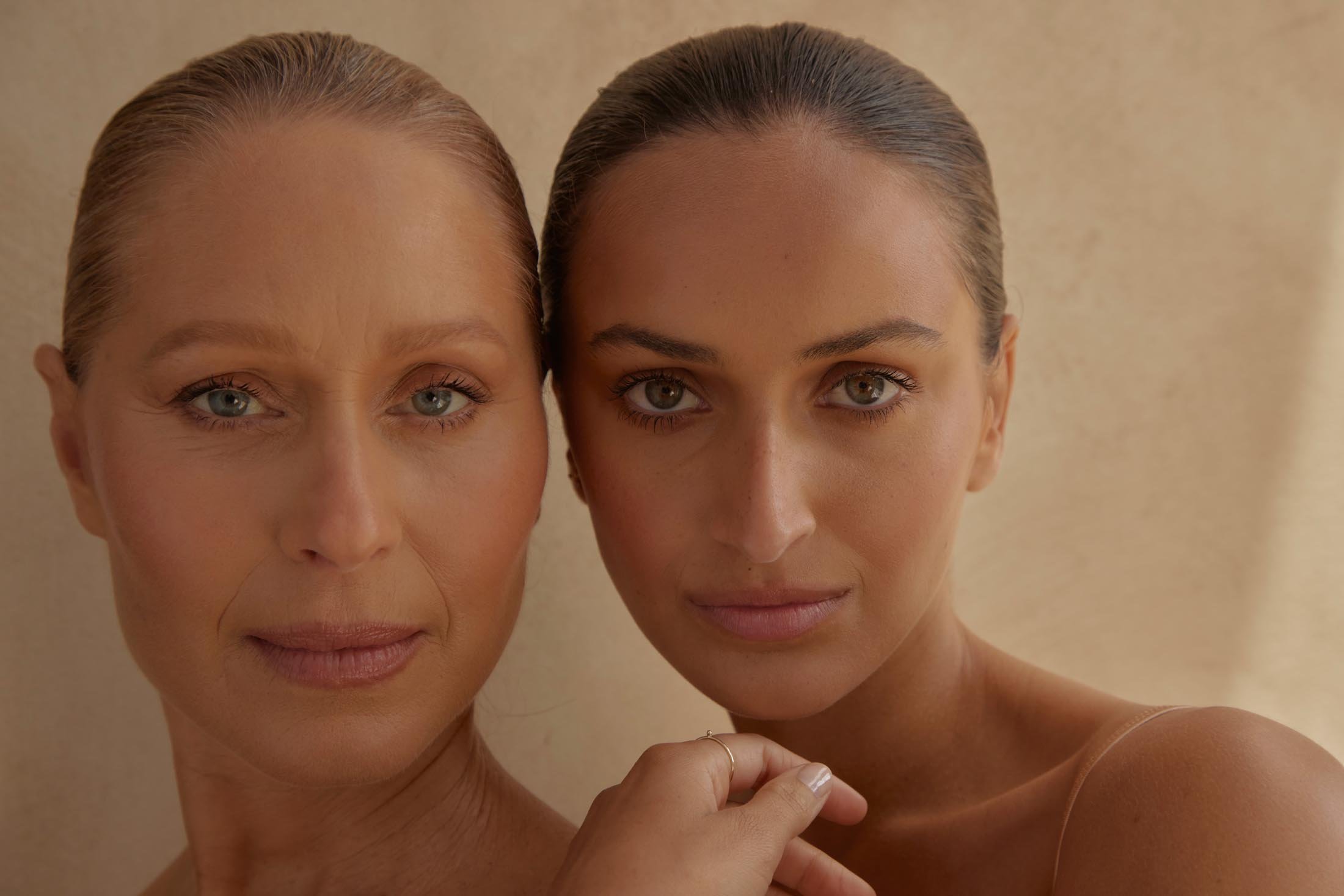 Close-up portrait of two women, an older woman and a younger woman, with neutral makeup and light skin tones, posing in a bright setting.