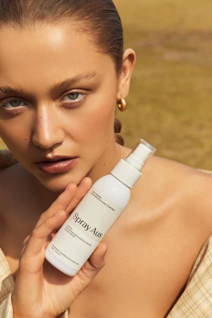 Close-up of a woman holding a white spray bottle in an outdoor setting, showcasing skincare product for beauty and cosmetic advertising.