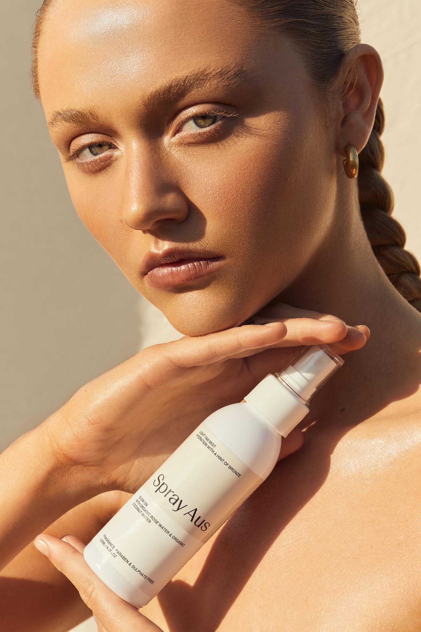 Close-up beauty portrait of a woman holding a white spray bottle of skincare product, styled by Max May.