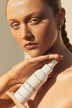 Close-up beauty portrait of a woman holding a white spray bottle of skincare product, styled by Max May.