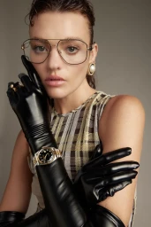 Close-up portrait of a woman wearing oversized wire-rimmed glasses, black leather opera gloves, and a wristwatch.