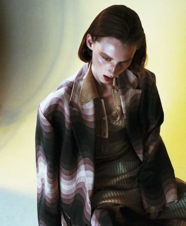 A woman in a wavy patterned blazer and matching dress posing against a gradient yellow and grey background.