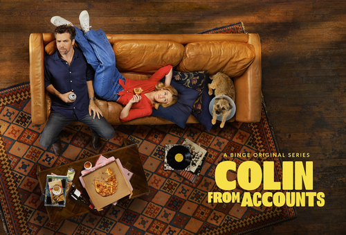Promotional shot from above of the television show Colin From Accounts, featuring two actors, a dog, pizza, vinyl records, and furniture.