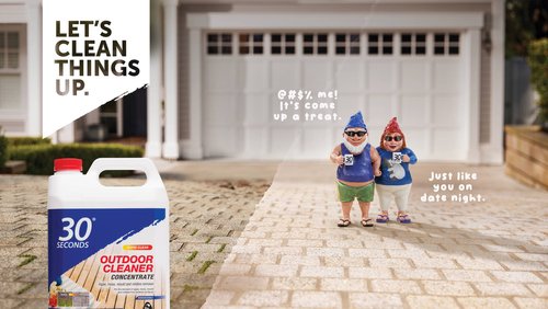 Outdoor cleaner concentrate advertisement featuring garden gnome figurines on a brick walkway leading to a suburban home.