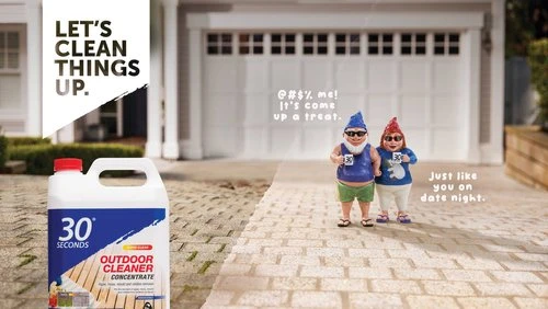 Outdoor cleaner concentrate advertisement featuring garden gnome figurines on a brick walkway leading to a suburban home.