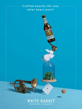A still life featuring a beer bottle, bell, rabbit figurine, playing card, trumpet, and a glass dome with greenery on a blue background.