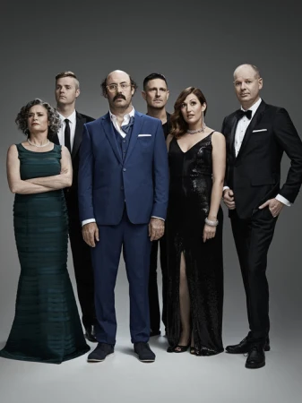 Group portrait of six formally dressed adults, three men in suits and bowties, one man in a blue suit, and two women in gowns.