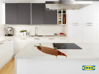 Spilled coffee on a white kitchen island countertop next to a knocked over cup in a modern kitchen