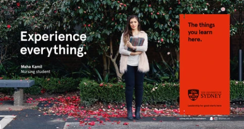 A young woman standing outdoors on a paved ground with fallen red flowers, holding a book, with dark shrubs in the background.