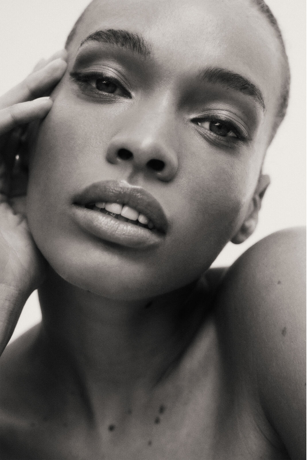 Close-up black and white portrait of a beautiful African American woman with hands near her face, looking at the camera.