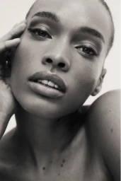 Close-up monochrome portrait of a woman with short hair resting her hand on her cheek against a neutral light background.