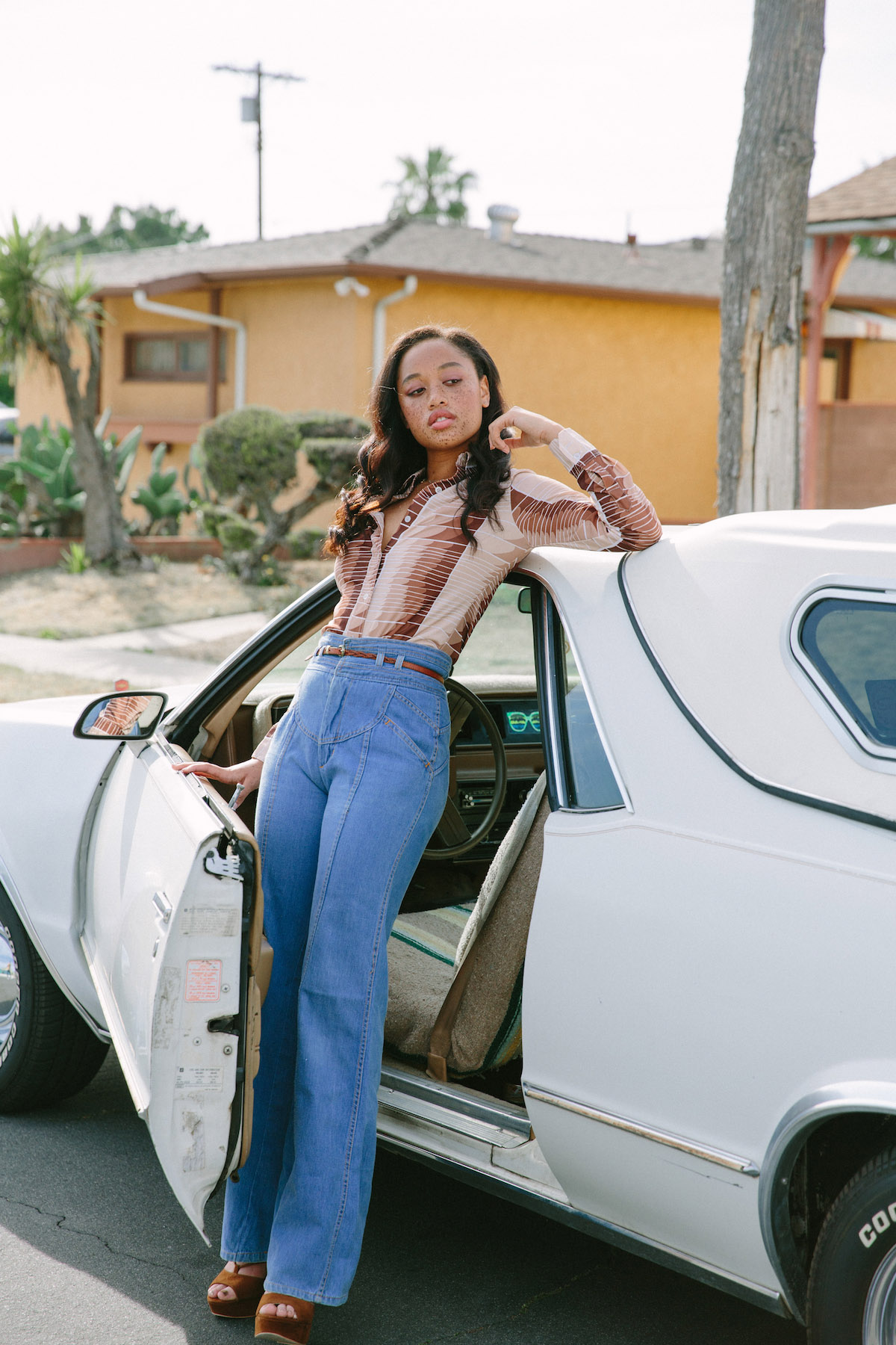 Young woman in retro outfit poses with vintage car on suburban street, warm light, stylish and fashionable.