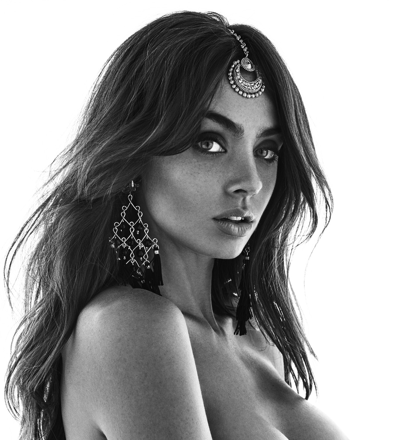 Monochromatic portrait of a woman with long brown hair wearing a jeweled headpiece and earrings against a bright white background.