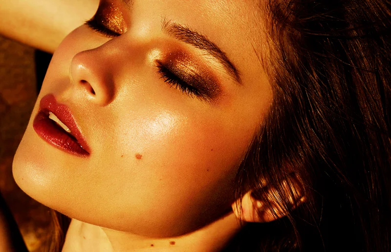 Close-up portrait of a woman with glowing skin, golden eyeshadow, and glossy red lips shot by Casey Gore in Sydney
