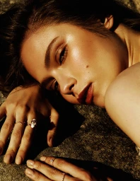 Close-up portrait of a woman resting her head on a textured stone surface, illuminated by warm sunlight.