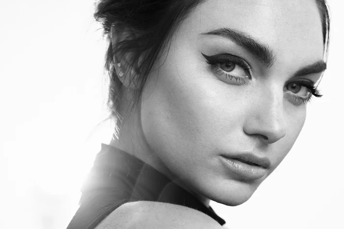 Close-up portrait of a woman with winged eyeliner and styled hair against a bright white background