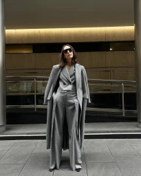 Woman in a grey suit and matching long coat wearing sunglasses standing outdoors in Sydney by Marina Didovich
