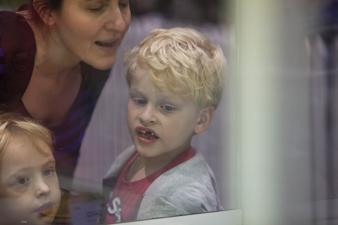 Close-up of a woman and two children looking out through a glass window with neutral colors and natural lighting indoors.