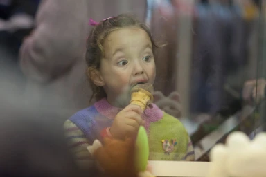 Young child eating a chocolate ice cream cone, captured through a glass barrier by photographer Penny Clay.