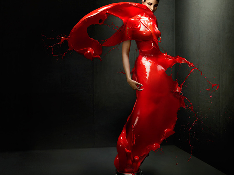 Woman in red liquid dress posing in studio against dark background. Dynamic action and striking visual art create a dramatic image.
