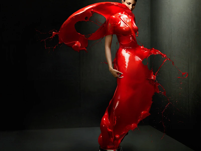 Woman in red liquid dress posing in studio against dark background. Dynamic action and striking visual art create a dramatic image.