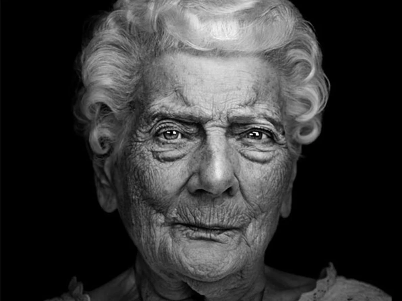 Monochrome portrait of a senior woman with curly white hair against a dark background showcasing the details of her face.
