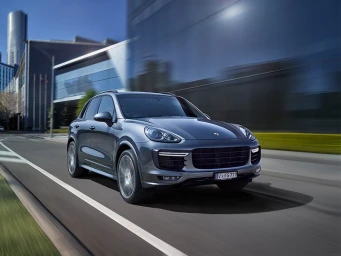 Grey luxury SUV driving on a city street past modern glass buildings with motion-blurred background.