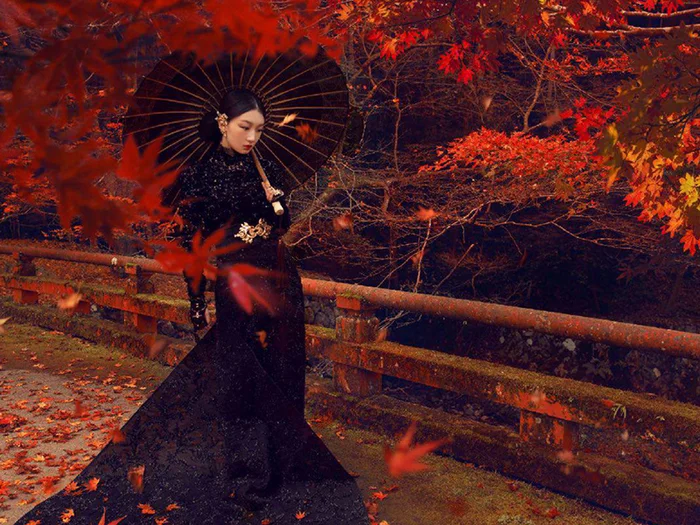 Woman in black gown holding an open umbrella on a red leaf strewn bridge in autumn produced by Adrian Appel