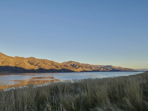 Scenic view of mountains and a lake reflecting the sky at sunset, with golden-brown grasses in the foreground, creating a tranquil landscape.