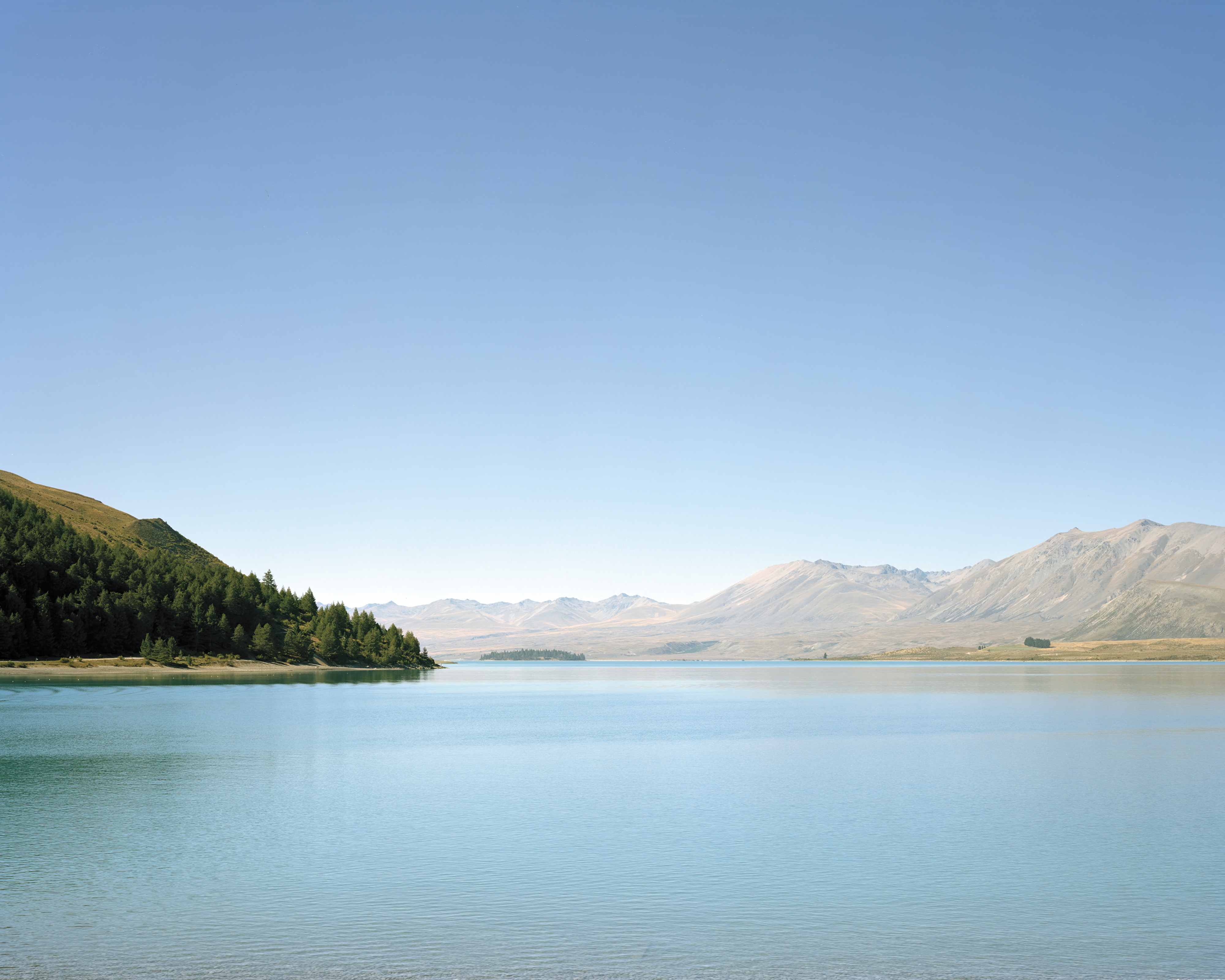 Scenic view of Lake Tekapo with turquoise water and mountain backdrop under a clear sky, showcasing New Zealand's natural beauty.