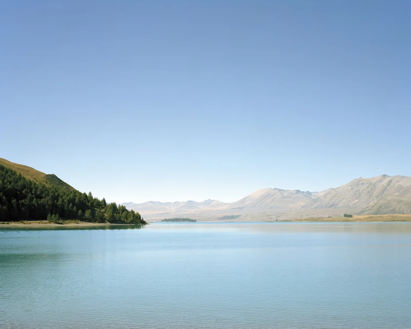 Scenic view of Lake Tekapo with turquoise water and mountain backdrop under a clear sky, showcasing New Zealand's natural beauty.