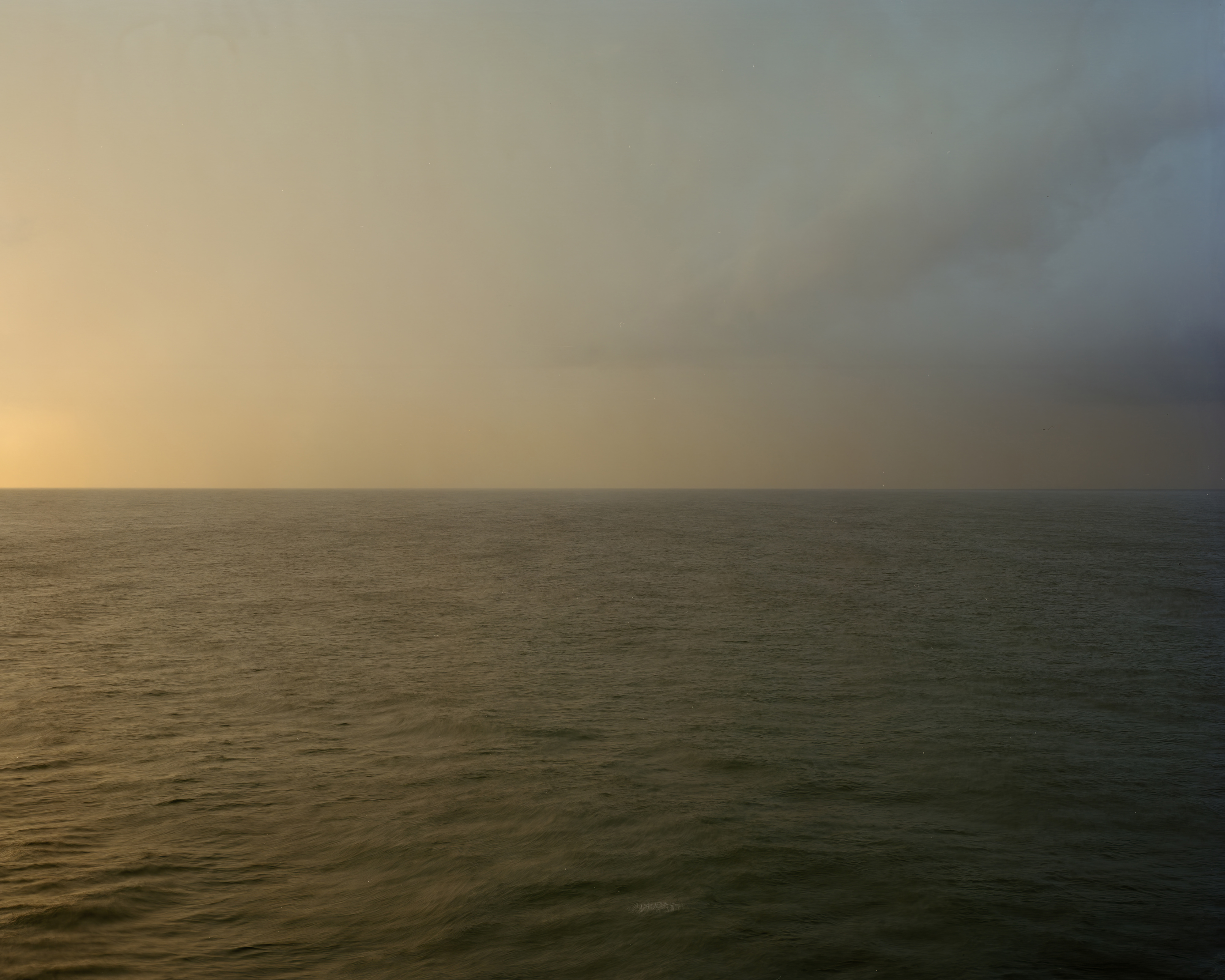 Scenic seascape view of the ocean water meeting a gradient sky with orange and blue hues at the horizon, captured in an outdoor setting.