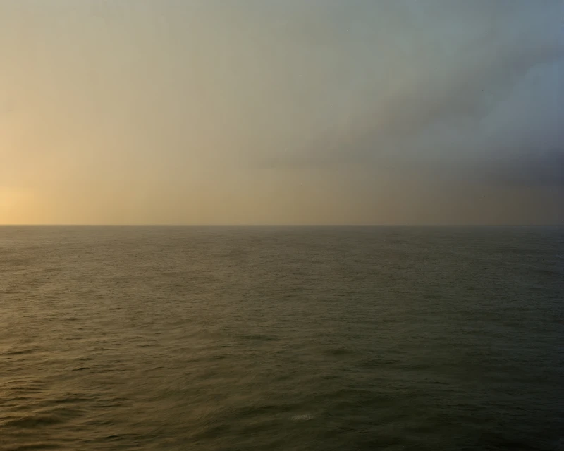 Scenic seascape view of the ocean water meeting a gradient sky with orange and blue hues at the horizon, captured in an outdoor setting.