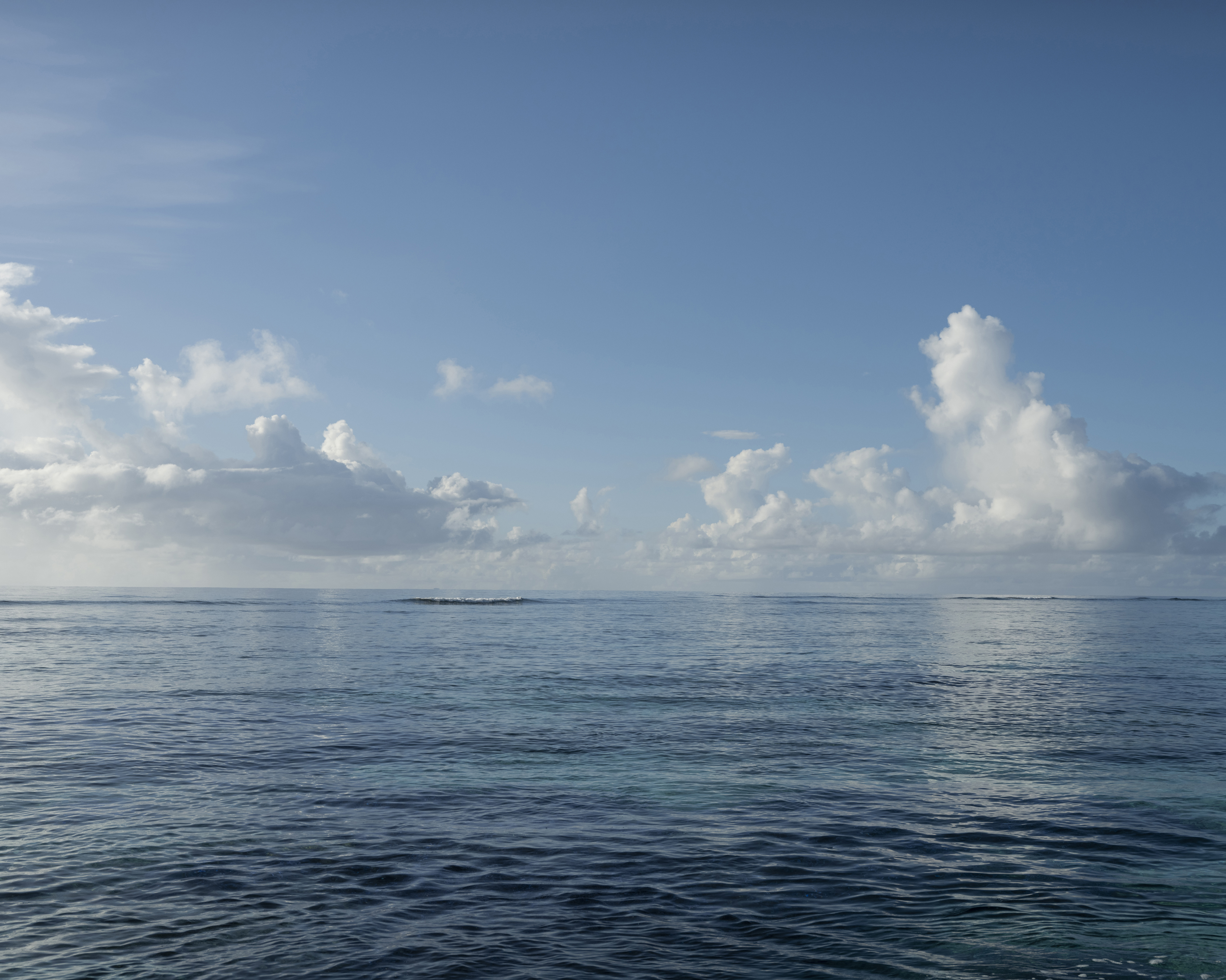 Tranquil ocean view with blue water and soft, white clouds against a blue sky, creating a serene and peaceful seascape.