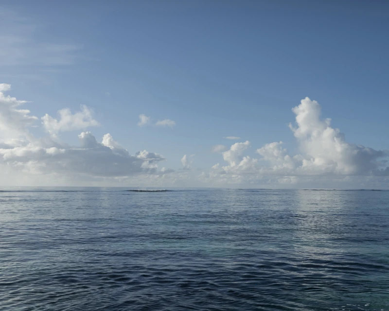 Tranquil ocean view with blue water and soft, white clouds against a blue sky, creating a serene and peaceful seascape.