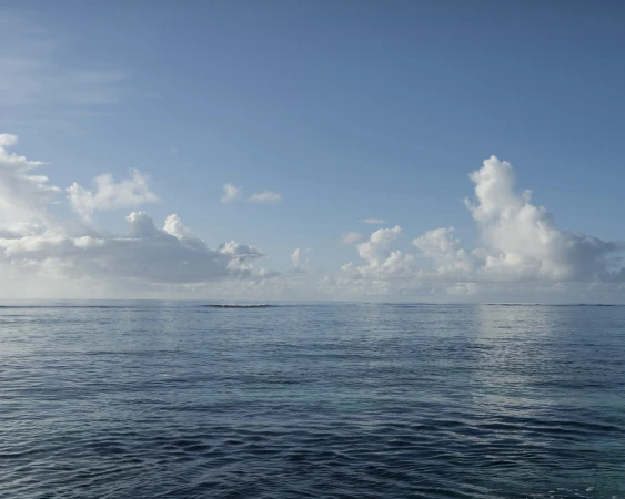 Tranquil ocean view with blue water and soft, white clouds against a blue sky, creating a serene and peaceful seascape.