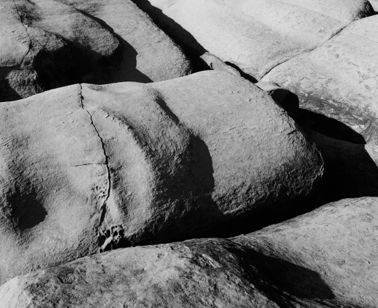 Black and white photograph showing weathered rock formations with deep crevices and strong shadows by Derek Henderson