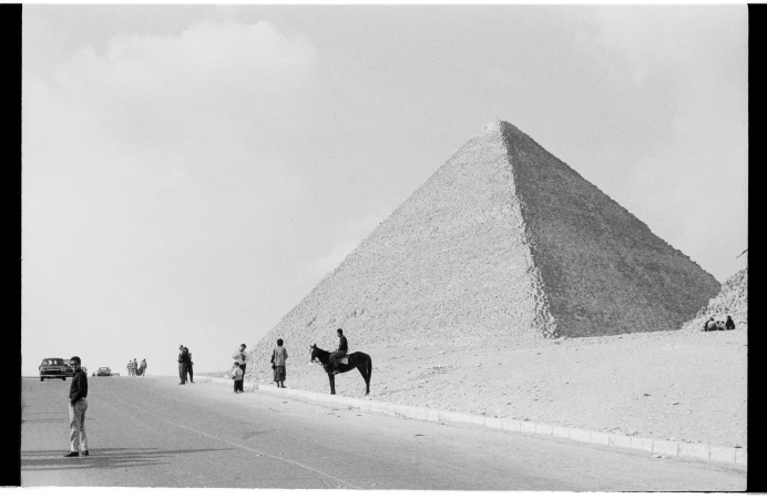 Black and white photograph of people near the pyramids of Giza, Egypt with a man riding a horse in a desert environment.