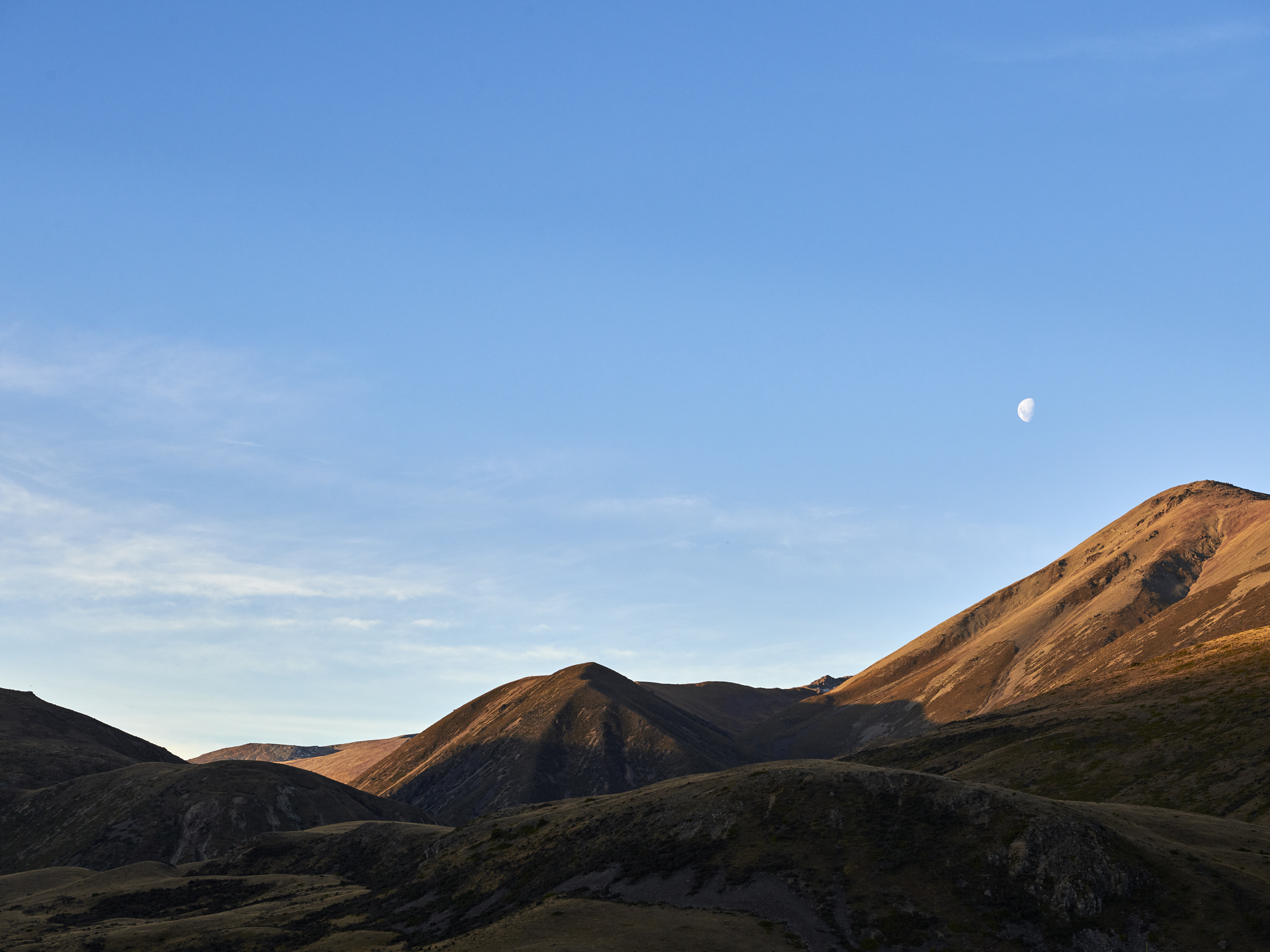 A scenic landscape features rolling hills under a clear blue sky with a partial moon visible, evoking a sense of tranquility and natural beauty.