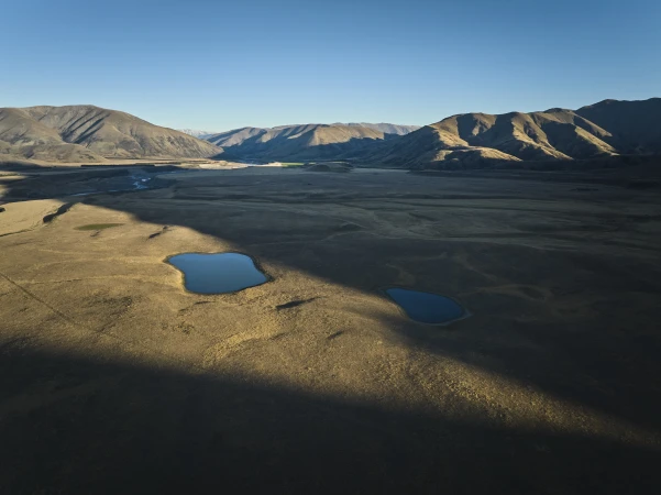 Aerial landscape photograph showing two small blue lakes in a vast dry valley surrounded by rolling mountains under a clear blue sky.