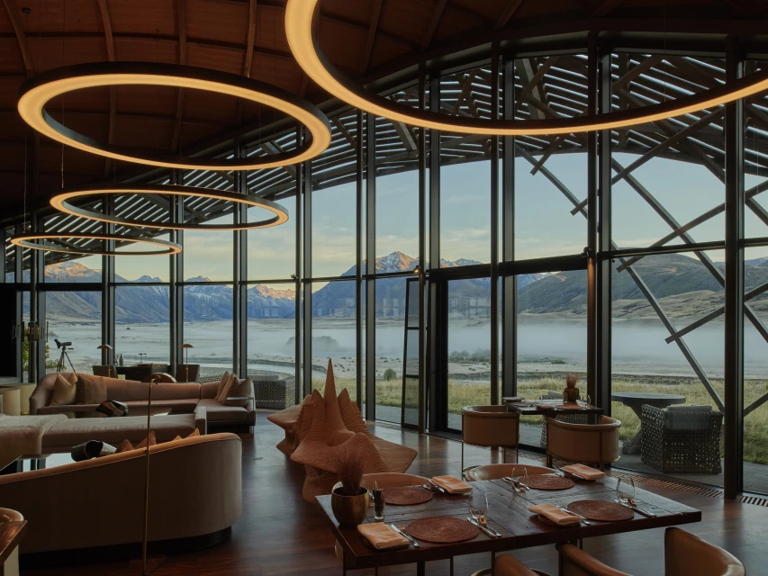 Interior view of a modern dining and lounge area featuring large windows, contemporary furniture, and mountain views in the background.