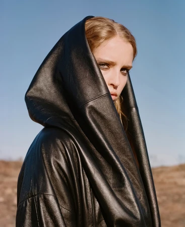 Close-up portrait of a woman in a black hooded leather coat against a clear blue sky by photographer Derek Henderson.