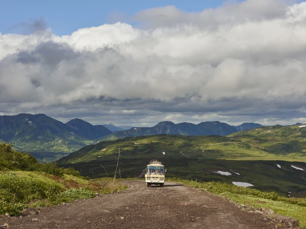 A vintage bus travels on a dirt road through a hilly landscape with cloudy skies, showcasing travel and adventure in nature.