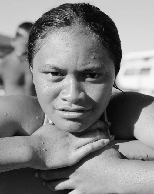 Monochrome portrait of a young adult woman with wet hair and water droplets on her skin, resting chin on hands, looking at the camera.