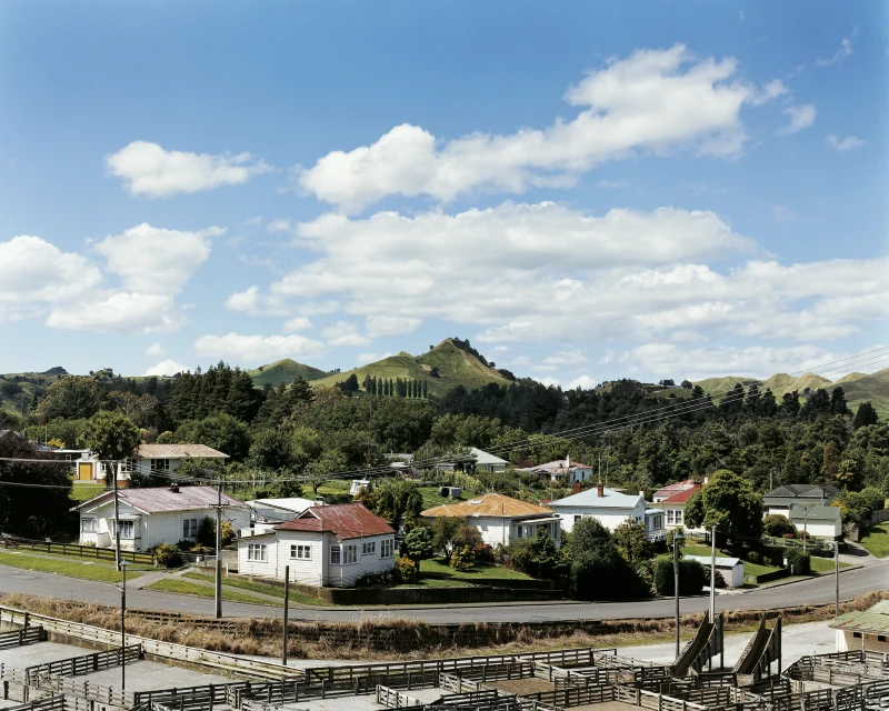 Residential neighborhood nestled in rolling hills under a bright blue, partially cloudy sky, offering a tranquil view of homes and nature.